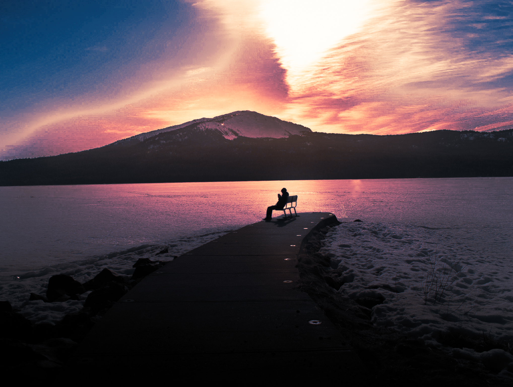 A person sitting on a bench reading on Diamond Lake in Oregon.