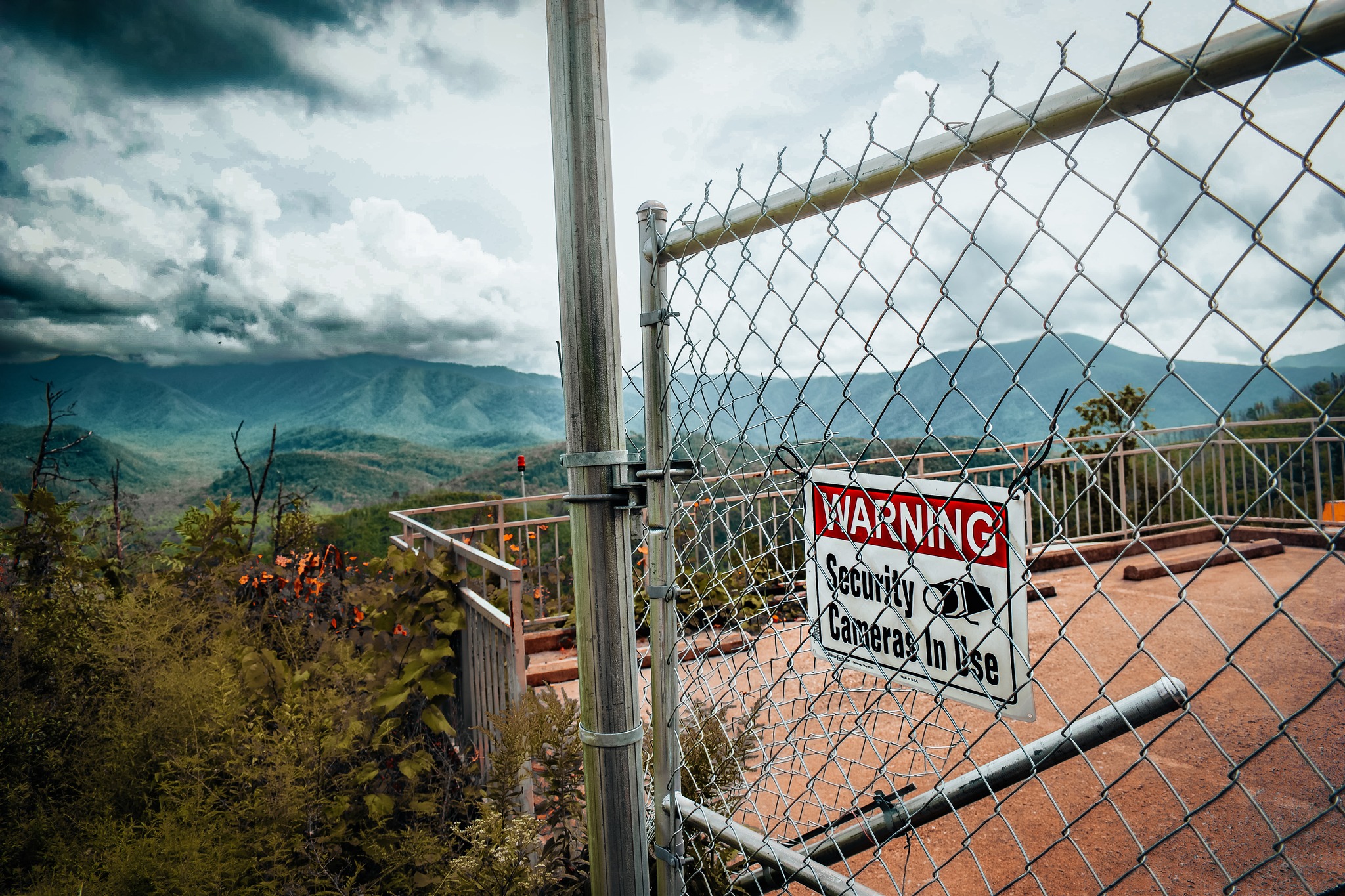 An image taken off the side of the road with a warning sign on a fence.