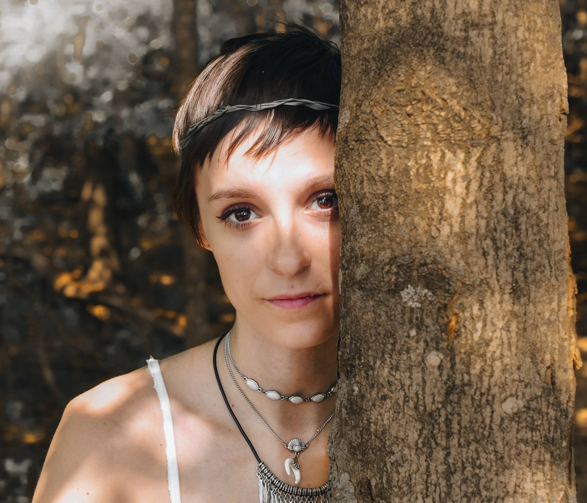 A portrait of a woman standing behind a tree.