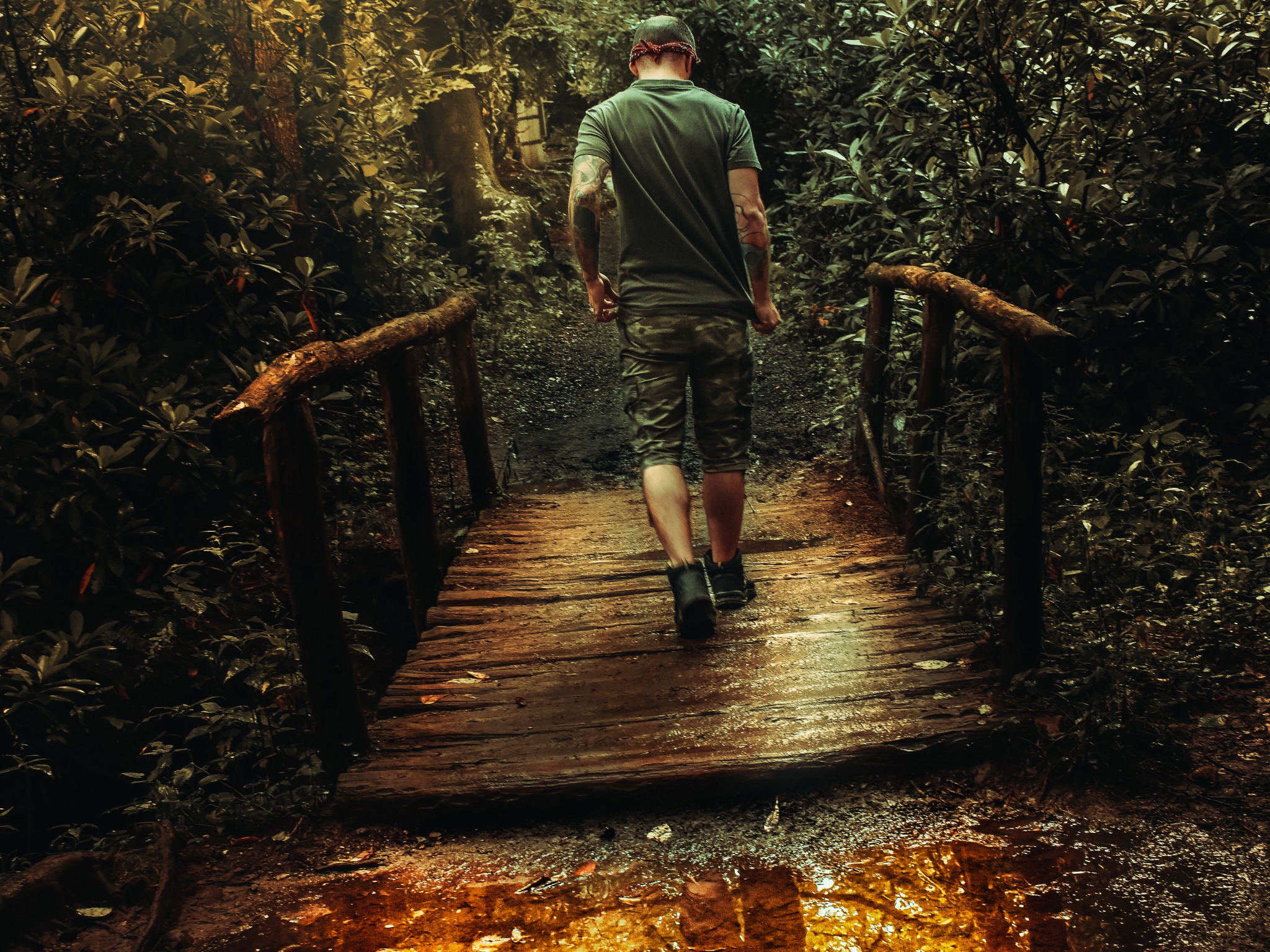 A man crosses a bridge as his reflection passes through a puddle.